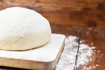 Ball of pizza dough on a rustic wooden background with dusting of flour