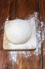 Ball of pizza dough on a rustic wooden background with dusting of flour