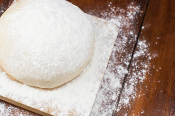 Ball of pizza dough on a rustic wooden background with dusting of flour