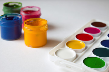 Multi-colored gouache in plastic jars, watercolor paints and art brushes on a white background...