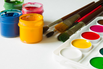 Multi-colored gouache in plastic jars, watercolor paints and art brushes on a white background close-up and copy space