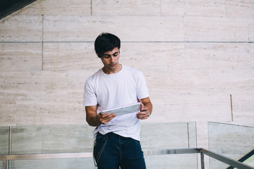 Serious caucasian male millennial reading information on browsed web page on digital tablet on free...