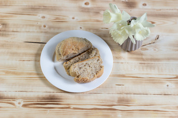 bread slices in white plate on a wooden table and daffadils in vase