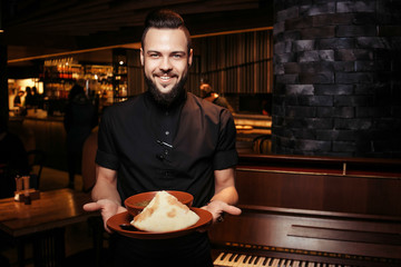 Cheerful bearded waiter with rich tomato soup with beef, rice. A discerning waiter in black clothes, with a beard and a tomato soup