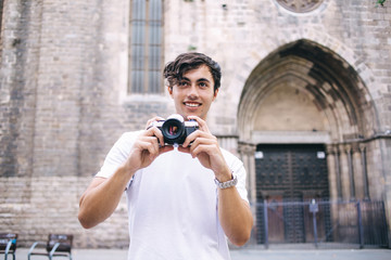 Happy positive male with camera having trip and exploring town on vacation holidays making photos, smiling hipster guy 20s visiting city and taking pictures spending free time on leisure outdoors