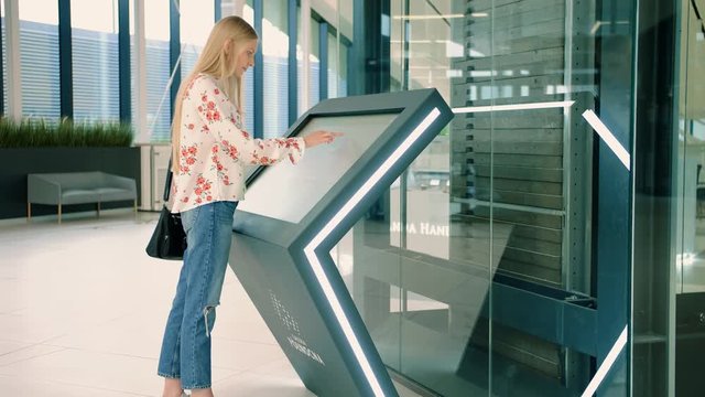 Woman near navigation board in mall. Side view of lovely young female in casual outfit looking for right direction on navigation board in modern mall.