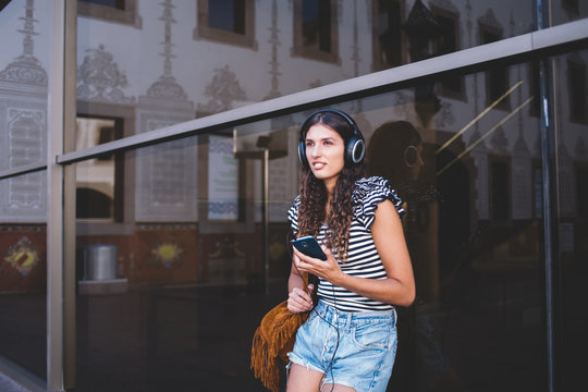 Young woman with headphones and mobile phone resting on street