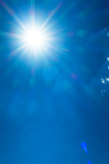 Shining sun with bokeh light & sunlight ray flares on beautiful sunny blue sky background in tropical summer or spring midday at daylight sunshine day, solar energy concept