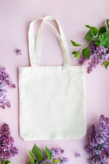 Eco tote bag lying on the pink background with beautiful lilac flowers