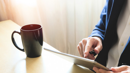 Man business person with suit using tablet device reading news or check for financial stock exchange information while drinking coffee in the morning at the cafe or office. with copy space for text