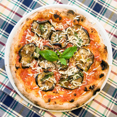 a real italian vegetable pizza in a dish, egg plant cheese and basil view from the top on a plaid tablecloth