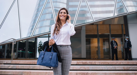 Cheerful elegant businesswoman talking on mobile against commercial buildings