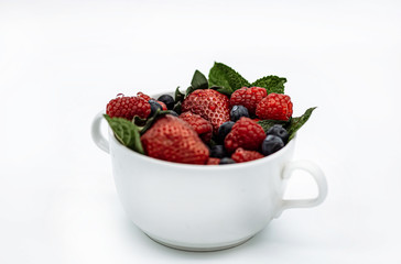 Summer berries in a cup strawberries, mint, raspberries, blueberries on a white background