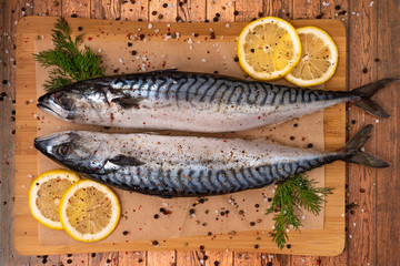 Two fresh mackerels on parchment paper on a cutting Board marinated in spices and lemon, decorated with herbs.
