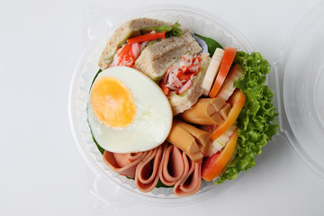 Salad, fried egg, bacon, tomato is packed in a circular plastic box