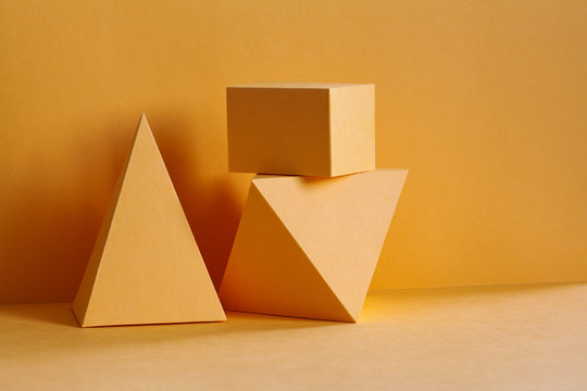 Yellow geometrical platonic solids figures still life composition, simplicity concept. Three-dimensional prism pyramid rectangular cube objects on yellow background.
