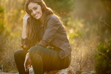 Girl with brown hair sitting on a stone smiling