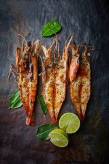 grilled langoustines on black slate with leaves and lime slices, bbq langoustines with lime and garlic, summer barbecue, seafood restaurant menu, top view, copy space, vertical image   