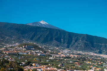 Landscape of the city of Puerto de La Cruz and the Teide volcano on a Sunny day under a blue sky. Tropical island with a volcano near the city