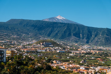 Landscape of the city of Puerto de La Cruz and the Teide volcano on a Sunny day under a blue sky. Tropical island with a volcano near the city