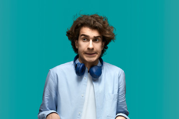 It looks like they will punish me. Portrait of a young beautiful man wearing white t-shirt and blue shirt in headphones awaiting punishment for his actions