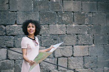 Cheerful black tourist reading map near old wall
