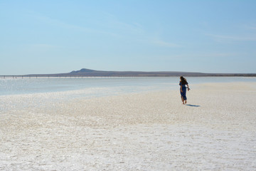 Fototapeta na wymiar Salt lake Baskunchak, Astrakhan region, Russia. A girl in a blue dress is walking along a salt lake.