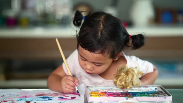 Little asian girl drawing in book on table indoor.