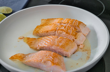 Bio Lachsfilet auf der Haut gebraten in einer weißen Pfanne mit Zitronen- und Limettenscheiben