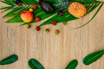 Flat lay, top view, Mix of Exotic fruits and palm leaf on a brown background: pineapples, Avocado, mangoes, mangosteen, lychee, citrus fruits