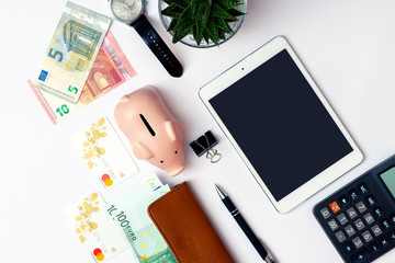 Top view image.Piggy bank, office supplies,pen, credit cards,calculator, clock and money on a white desk.