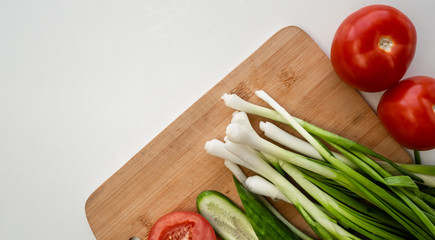 Fresh herbs, onions, parsley, tomatoes, cucumber lie on a wooden board for making salad.