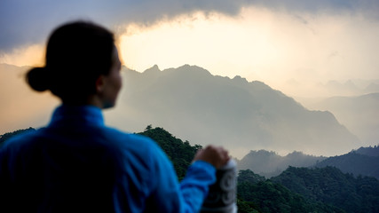 A young beautiful girl in a blue wind proof jacket from the back watching a sunrise over the mountains, travel, trekking and hiking concept, nature at the national park