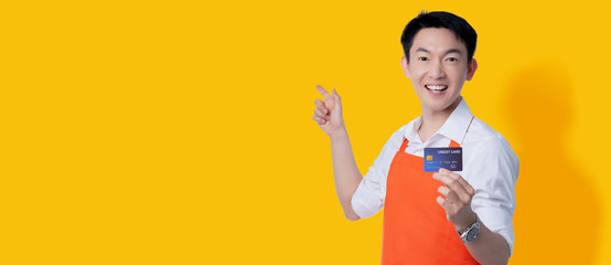 asian attractive male business owner apron uniform hand gesture point finger with confident hand hold credit card business online payment technology business new promotion ideas