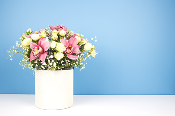 Vase with beautiful bouquet of orchids, roses and gypsophila, Baby's-breath flowers, on white table with trendy blue background with copy space for your text. Selective focus, celebrating concept
