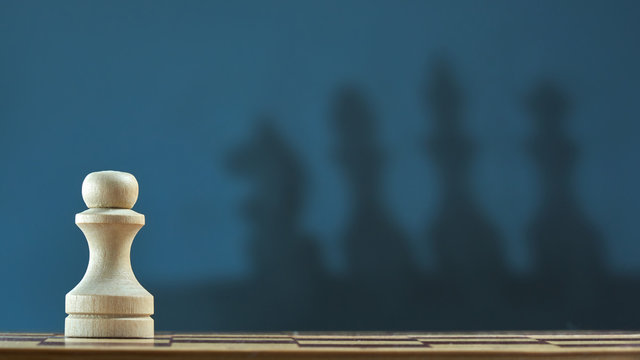 Chess pawn with blur shadow of king, Queen, horse on a dark gray background. Photo with copy space.