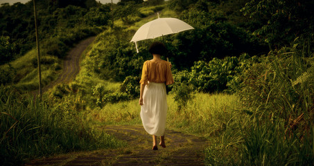 A girl in a white dress on the path of the artist. Girl with an umbrella. Bali trip. Tropics. Campuhan Ridge Walk Travel.