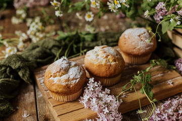 Fototapeta na wymiar On the table among the lilac branches are vanilla cupcakes