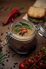 Glass jar with poultry pate, decorated with almonds and rosemary with cocktail tomatoes and hot pepper on a wooden table
