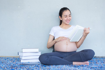 A pregnant mother is reading a book about raising children in the living room.