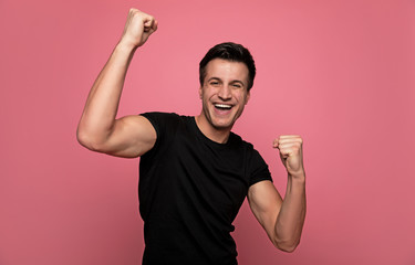 Fototapeta premium Sports fan. Close-up photo of a sporty young man in a black t-shirt, who is holding his hands in fists and smiling.