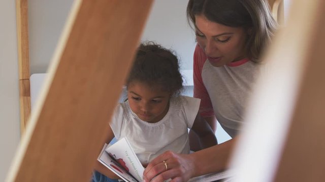 Hispanic mother and daughter sitting on girls bunk bed at home reading book together - shot in slow motion