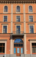 Fototapeta na wymiar House facade with light brown walls. Classic city architecture with decorative windows in row in downtown Saint Petersburg, Russia. Apartment modern building entrance, straight house facade view