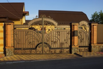 brown metal gate with forged pattern and part of a brick fence on the street on a sunny day