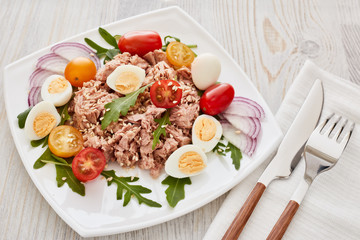 Tuna salad with arugula and tomatoes on light wooden background. Healthy food, seafood menu,