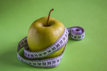Green apple with measuring tape on green background. Concept of healthy lifestyle and diet