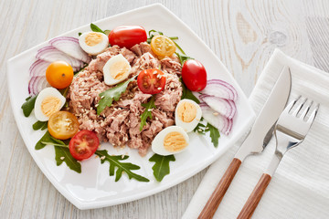 Tuna salad with arugula and tomatoes on light wooden background. Healthy food, seafood menu,