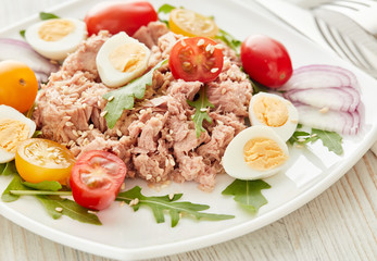 Tuna salad with arugula and tomatoes on light wooden background. Healthy food, seafood menu,