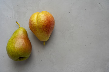 Two whole ripe pears are laying on the left side on cement surface