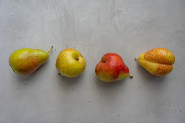 Four ripe whole pears are arranged in a horizontal line on a cement surface